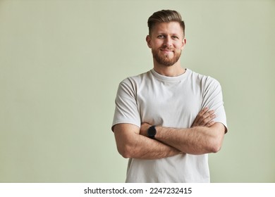 Waist up portrait of bearded young man smiling at camera while standing with arms crossed against pastel green, minimal - Powered by Shutterstock