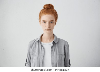 Waist up portrait of beautiful European 20 y.o. woman with freckles and hair knot posing isolated against grey studio wall background with copy space for your text, having calm expression on her face