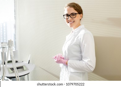 Waist up portrait of beautiful female cosmetologist smiling looking at camera and posing in sunlit modern SPA salon standing by wall, copy space