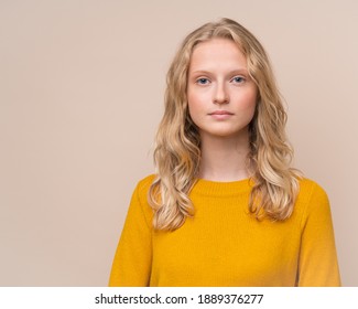 Waist Up Portrait Of Beautiful Young Serious Clever Blonde Scandinavian Woman Without Makeup On Beige Wall. Female With Fresh Face And Curly Hair In Bright Yellow Jumper, Teen In Orange Sweater