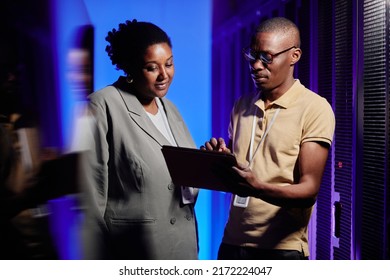 Waist up portrait of black adult man and woman using tablet in server room while setting up data network - Powered by Shutterstock