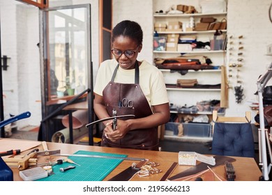 Waist up portrait of black female artisan punching holes in handmade belt in leatherworking shop, copy space - Powered by Shutterstock