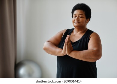 Waist Up Portrait Of Black Senior Woman Meditating With Eyes Closed While Doing Yoga Indoors