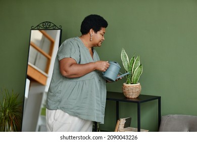 Waist up portrait of black senior woman watering houseplants at home, copy space - Powered by Shutterstock