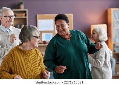 Waist up portrait of black senior woman dancing with friends in retirement home and smiling joyfully