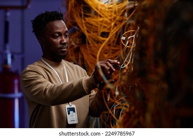 Waist up portrait of black young man as system administrator setting up server network and doing maintenance