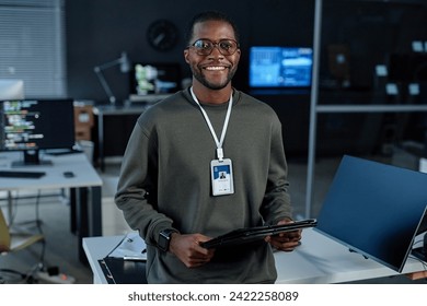 Waist up portrait of Black young man smiling at camera in cybersecurity office and wearing ID badge copy space - Powered by Shutterstock