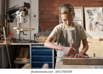 Waist up portrait of Caucasian girl measuring wooden board and building model in carpenting workshop - Powered by Shutterstock