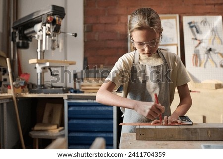 Waist up portrait of Caucasian girl measuring wooden board and building model in carpenting workshop