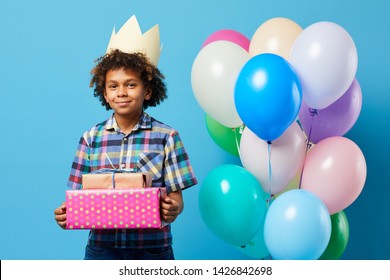 Waist up portrait of cheerful African-American boy holding presents posing against blue background, Birthday party concept, copy space - Powered by Shutterstock