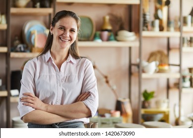 Waist up portrait of cheerful female artisan posing in pottery studio standing with arms crossed, copy space