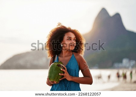 waist up portrait cheerful young brazilian afro hairstyle woman walking on the beach holding a coconut water in Ipanema 	