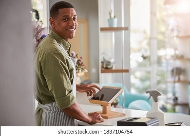 Waist Up Portrait Of Cheerful Young Handsome Man Selling Flowers And Standing At Counter With Tablet And Pos Terminal