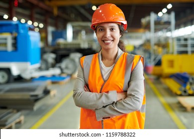Waist up portrait of cheerful young woman wearing hardhat smiling happily looking at camera while posing confidently in production workshop, copy space