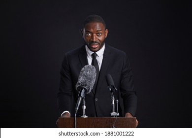 Waist Up Portrait Of Confident African-American Man Standing At Podium And Giving Speech Against Black Background, Copy Space