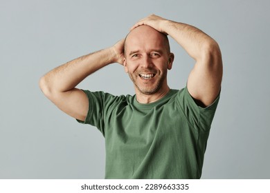 Waist up portrait of confident bald man smiling at camera and posing with hands on head - Powered by Shutterstock