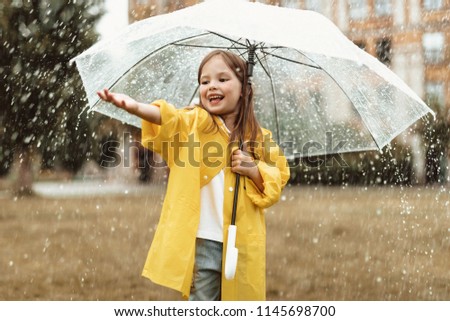 Waist up portrait of delighted young girl standing under umbrella with stretched hand. She is blissful to spend leisure outdoors