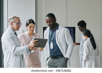 Waist up portrait of diverse group of doctors looking at digital tablet during council or conference - Powered by Shutterstock