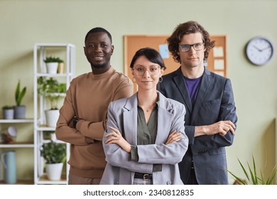 Waist up portrait diverse group of young people in office posing confidently with arms crossed and looking at camera