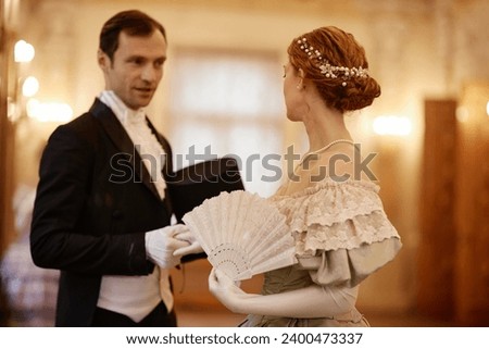 Waist up portrait of elegant couple of lady and gentleman talking in palace hall, copy space