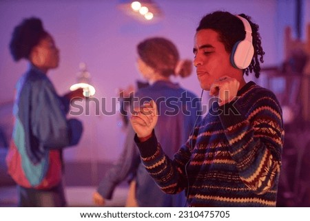 Waist up portrait of ethnic young man dancing with headphones on while enjoying silent disco party in neon light, copy space