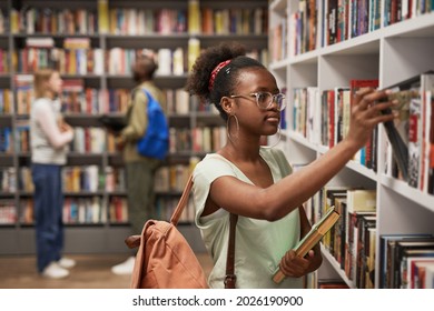Waist up portrait of female Africa-American student choosing books in college library, copy space