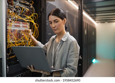 Waist up portrait of female network engineer connecting cables in server cabinet while working with supercomputer in data center, copy space - Powered by Shutterstock