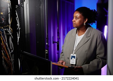 Waist Up Portrait Of Female System Engineer Setting Up Server Network In Neon Light And Using Laptop, Copy Space