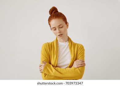 Waist up portrait of gorgeous young Caucasian woman with delicate features and ginger hair looking down with sad unhappy expression with arms crossed, feeling disappointed after quarrel with her man