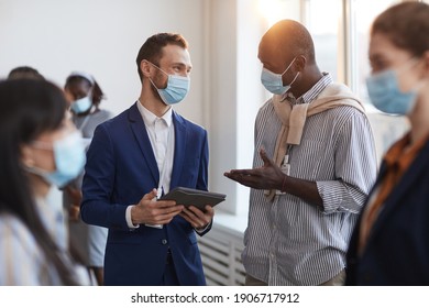 Waist Up Portrait Of Group Of People Chatting During Break At Business Conference, Focus On Two Men Wearing Masks With Lens Flare