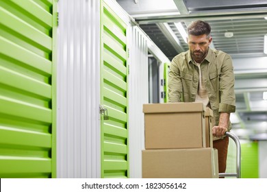 Waist up portrait of handsome bearded man loading cart with cardboard boxes into self storage unit, copy space - Shutterstock ID 1823056142