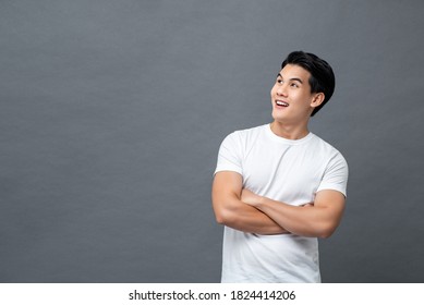 Waist up portrait of handsome cheerful Asian man in arm crossed gesture looking at empty space aside isolated gray background