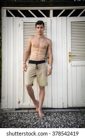 Waist Up Portrait Of Handsome Shirtless Smiling Young Man Leaning Out Of Cabana Door, Portrait Of Male Surfer Standing In Doorway Of Rustic Beach Hut