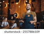 Waist up portrait of handsome waiter smiling cheerfully at camera standing in restaurant or cafe, copy space. Young waiter serving coffee in a cafe and looking at camera.