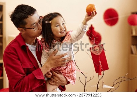 Waist up portrait of happy Asian girl holding tangerine while celebrating Chinese New year with father at home, copy space Have overflowing abundance every year
