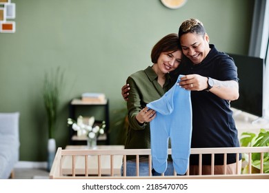 Waist Up Portrait Of Happy Gay Couple Expecting Baby And Preparing Crib With Baby Clothes At Home, Same Sex Family, Copy Space