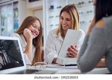 Waist up portrait of happy smiling pleasantly mother and funny daughter choosing and trying different eyeglass in ophthalmology cabinet
