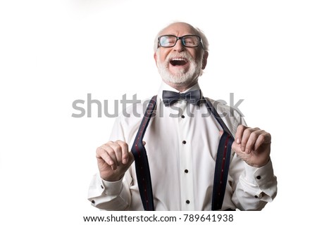 Waist up portrait of joyful old male pulling away his suspenders and laughing. Isolated on background