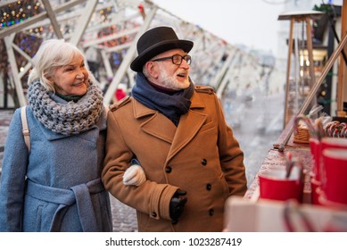 Waist up portrait of joyful senior man and woman are buying sweets in store outside. They are standing arm in arm and laughing. Holiday entertainment concept Stock Photo
