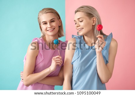Waist up portrait of laughing siblings wearing apparel holding sweets. Isolated on blue and pink background