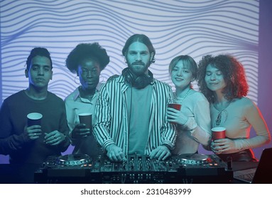Waist up portrait of long haired DJ with diverse group of people taking photo in nightclub lit by neon - Shutterstock ID 2310483999