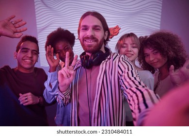 Waist up portrait of long haired man with diverse group of friends taking photo in nightclub lit by neon - Shutterstock ID 2310484011
