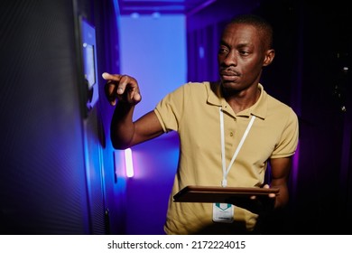 Waist up portrait of male system administrator setting up server network in data center lit by neon light