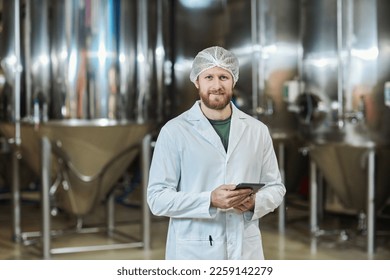 Waist up portrait of male worker wearing lab coat standing at food factory workshop and holding digital tablet, copy space - Powered by Shutterstock