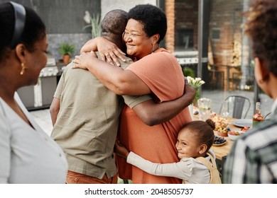 Waist up portrait of mature African-American woman embracing friend during family gathering at dinner party outdoors, copy space