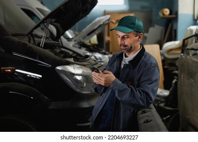 Waist Up Portrait Of Mature Male Worker Using Smartphone In At Car Factory Workshop