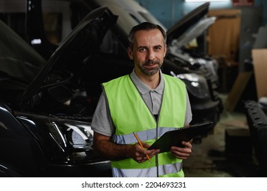 Waist Up Portrait Of Mature Male Worker Looking At Camera While Inspecting Vehicles At Car Factory Quality Control