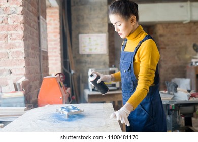 Waist Up Portrait Of Modern Young Woman Spray Painting Wood Piece While Working In Carpenters Workshop, Copy Space