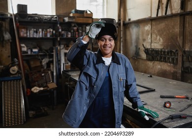 Waist up portrait of multiethnic female welder smiling at camera in industrial factory workshop, copy space - Powered by Shutterstock