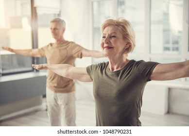 Waist up portrait of old jolly lady with arms straightened out aside. Male pensioner in same posture standing on background. Focus on woman - Shutterstock ID 1048790231